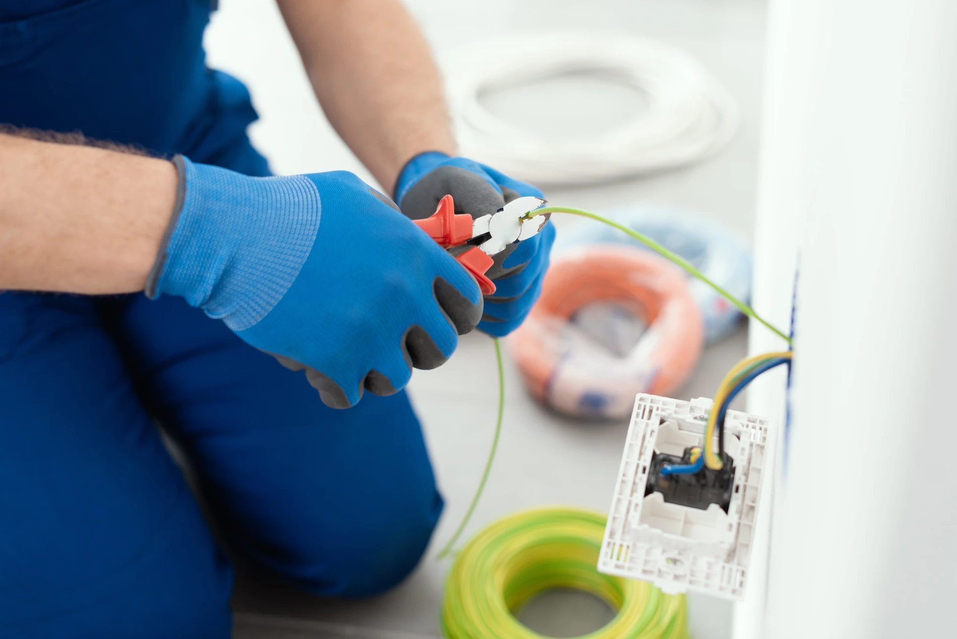 Électricien en tenue bleue effectuant des mesures électriques sur installation murale avec multimètre numérique orange
